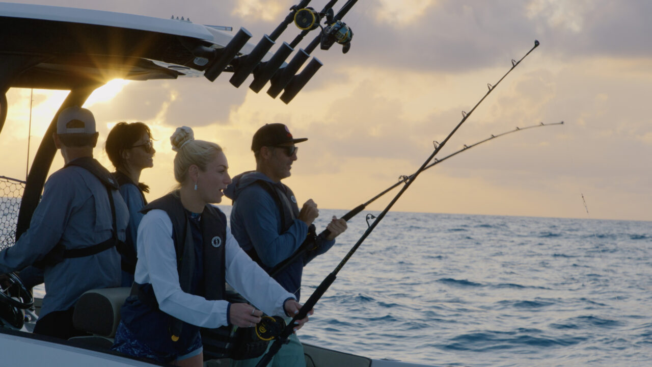 Two people fishing at sunset with rods extended over the water.